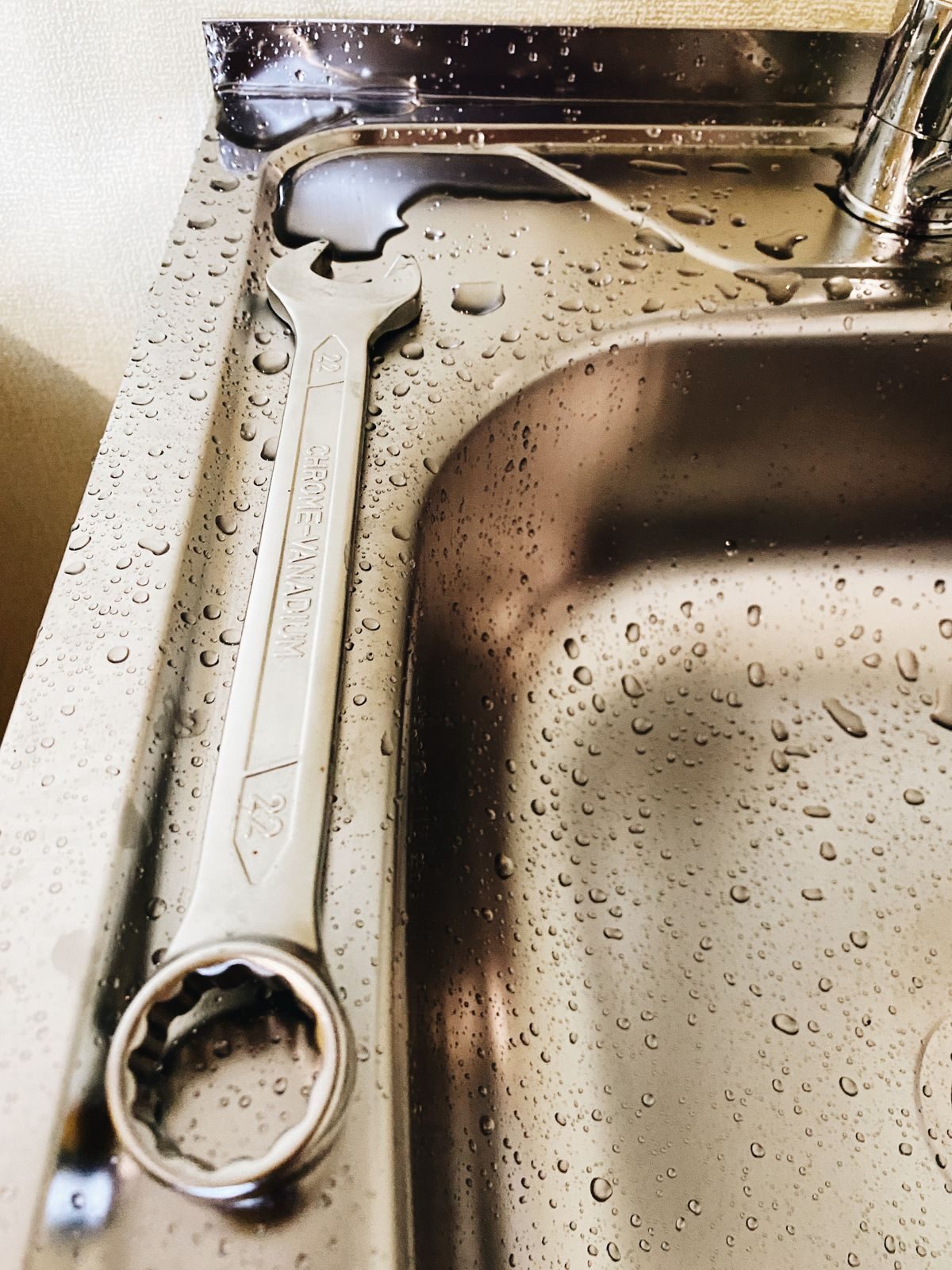 Wrench resting on a wet stainless steel sink during a leak repair